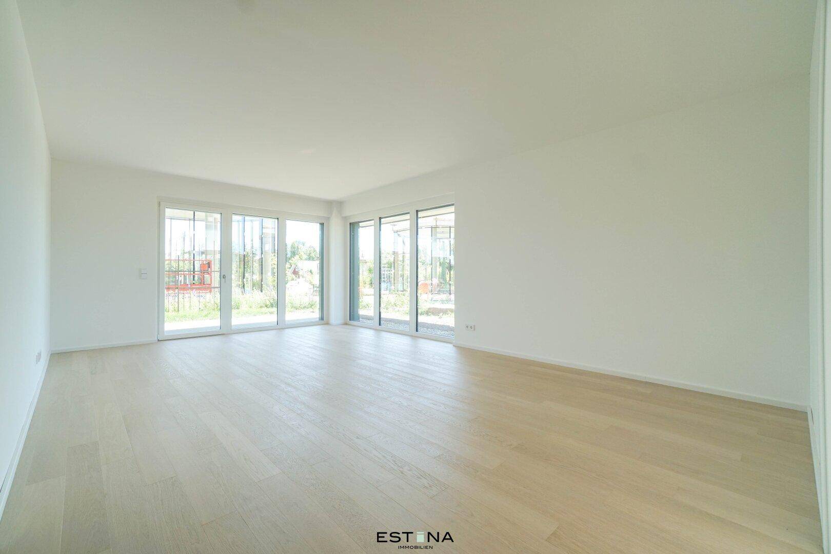 Helles, leeres Wohnzimmer mit großen Fenstern und hellem Holzparkettboden.