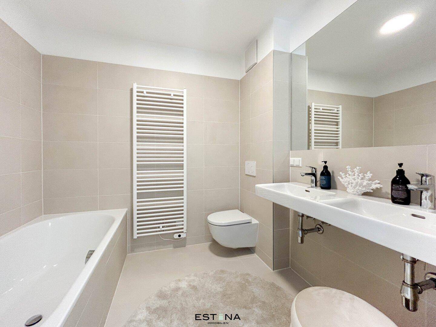 Modernes Badezimmer mit Badewanne, Doppelwaschbecken und beheiztem Handtuchhalter in hellen Farbtönen.