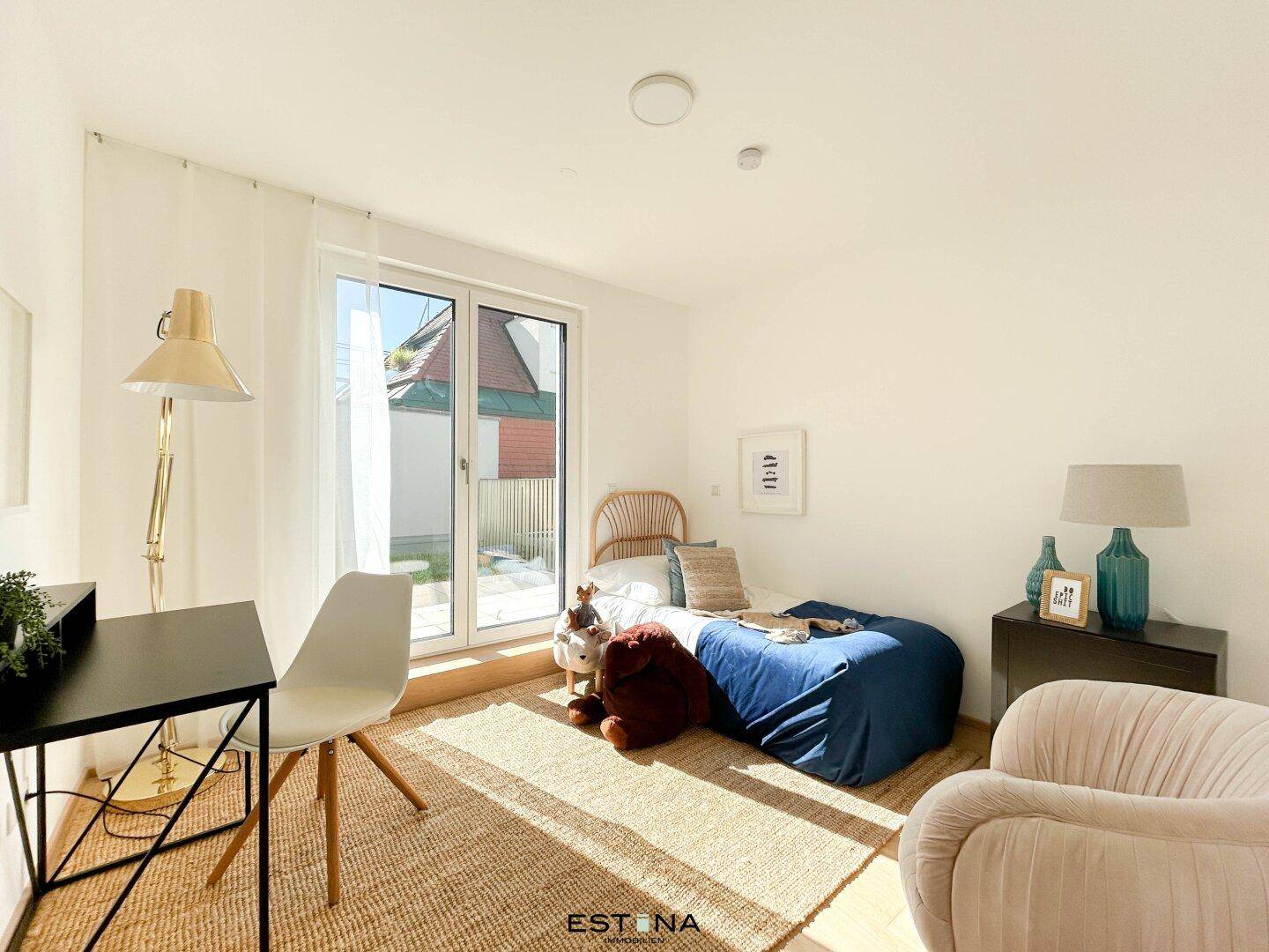 Freundliches Kinder- oder Gästezimmer mit Schreibtisch und Zugang zum Außenbereich durch große Fenster.