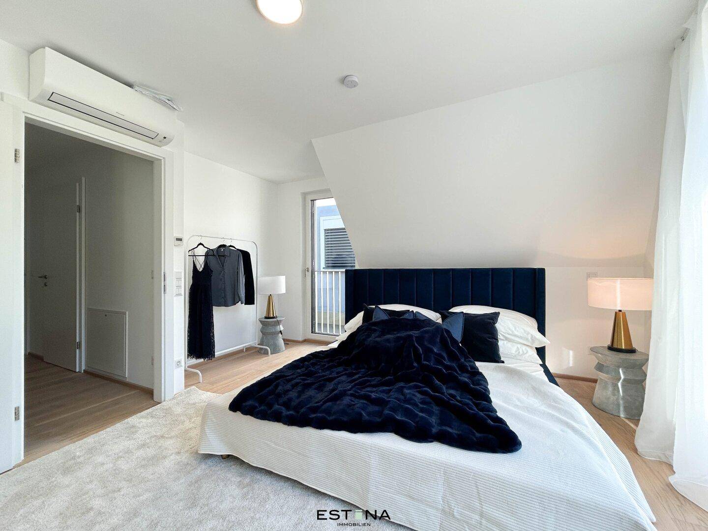 Modernes Schlafzimmer mit blauem Polsterbett, Holzboden und Klimaanlage unter Dachschräge.