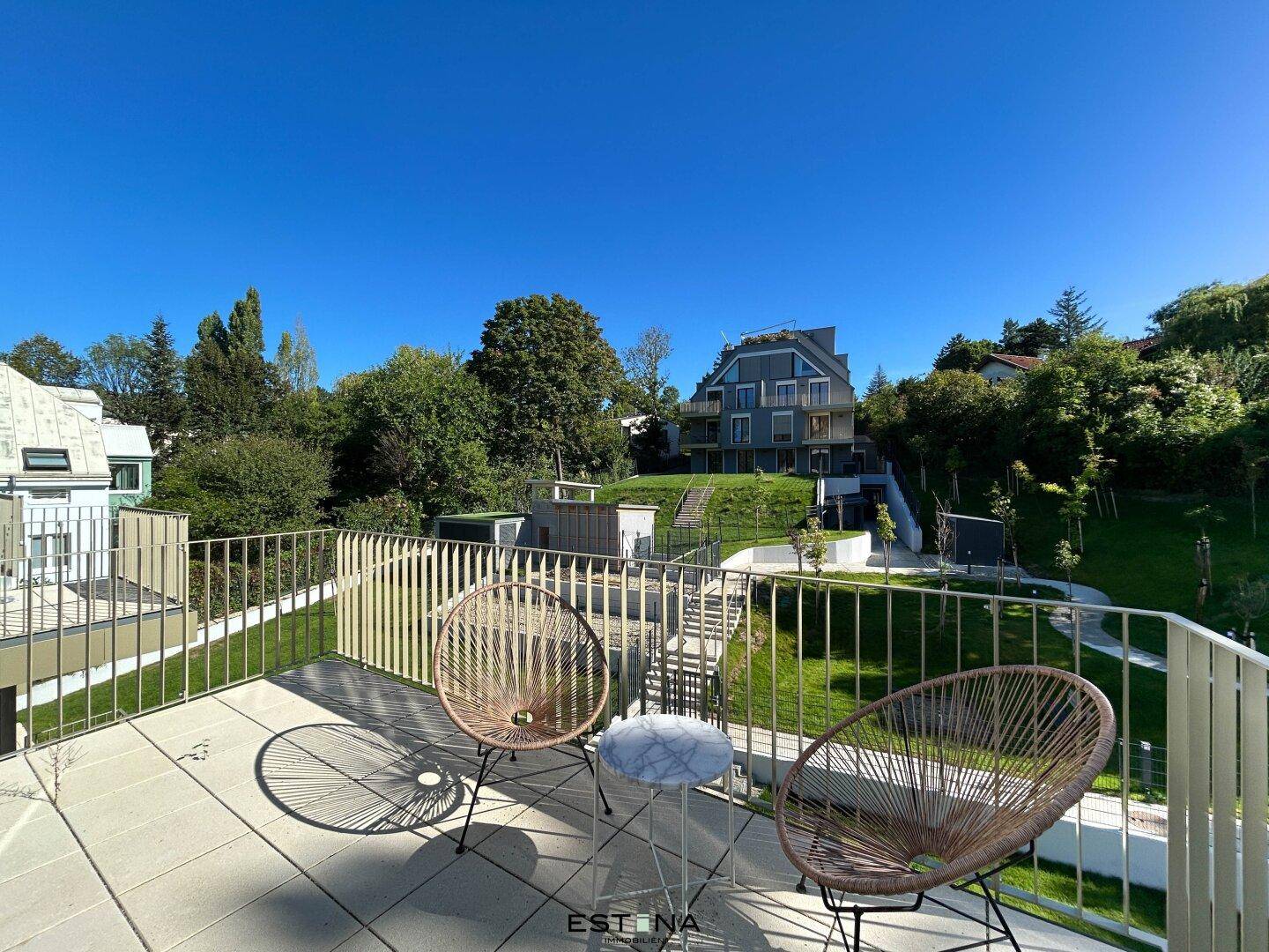 Sonniger Balkon mit Sitzgelegenheiten und Blick auf die grüne Umgebung und moderne Gebäude.