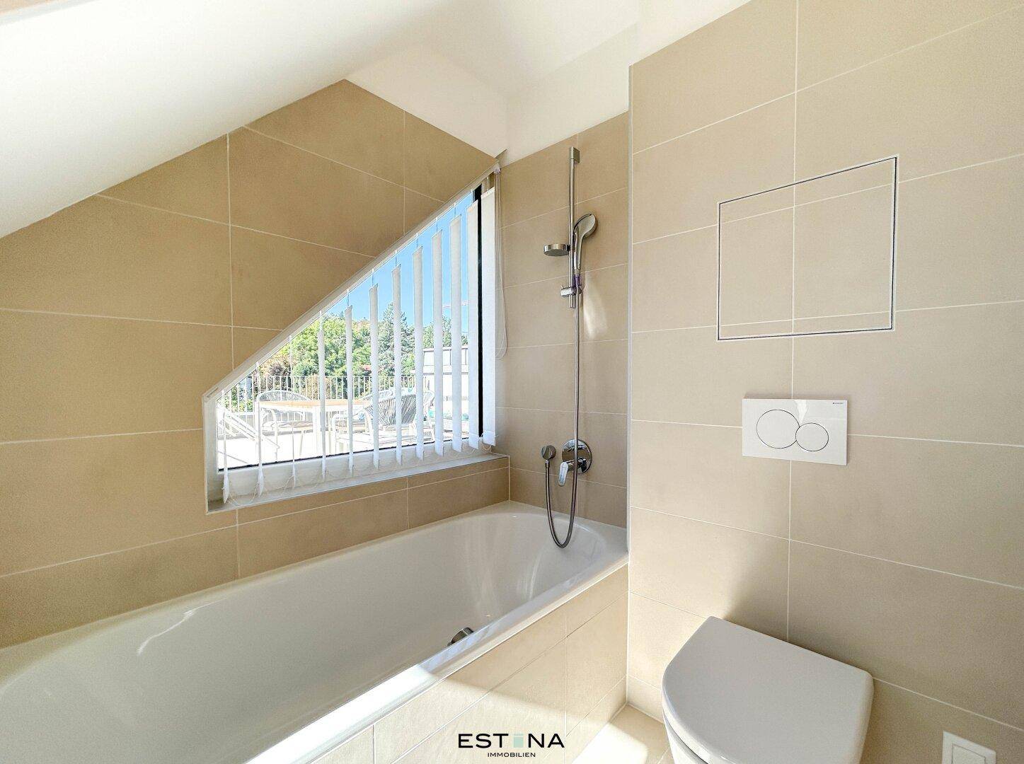 Helles Badezimmer mit Badewanne, Wand-WC und schrägen Wänden unter dem Dach.