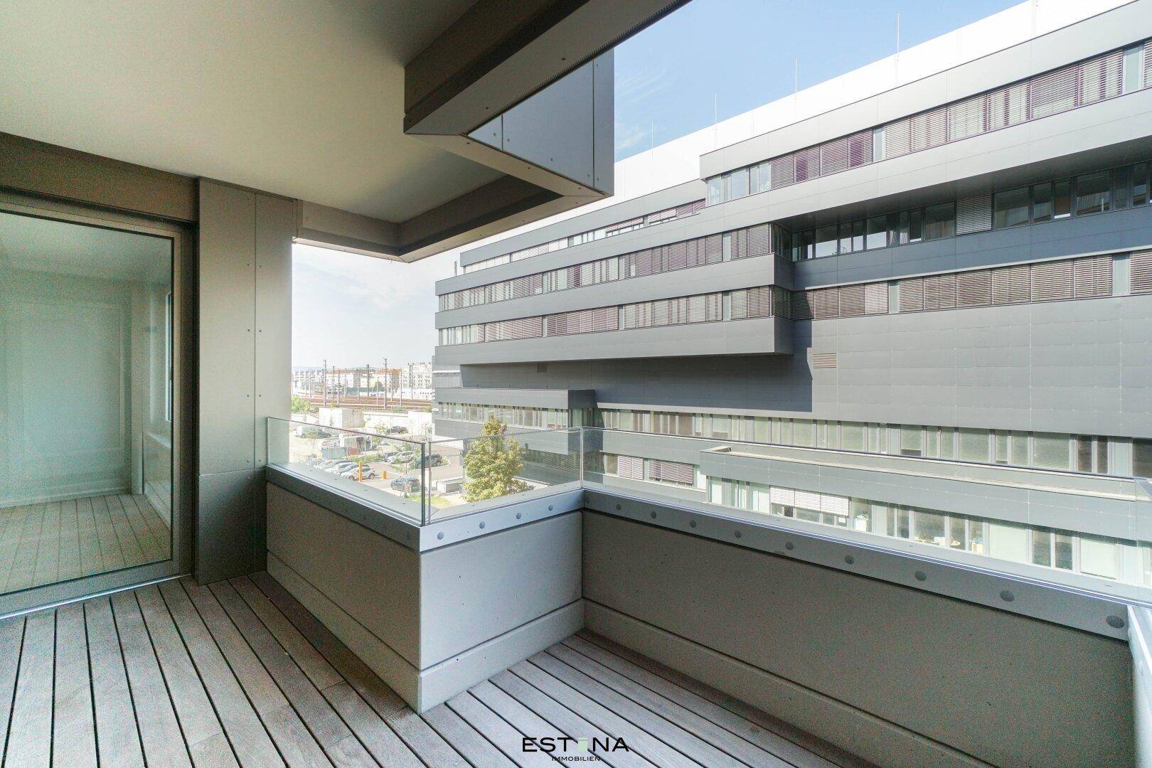 Moderner Balkon mit Holzboden, Glasgeländer und Blick auf die städtische Umgebung.