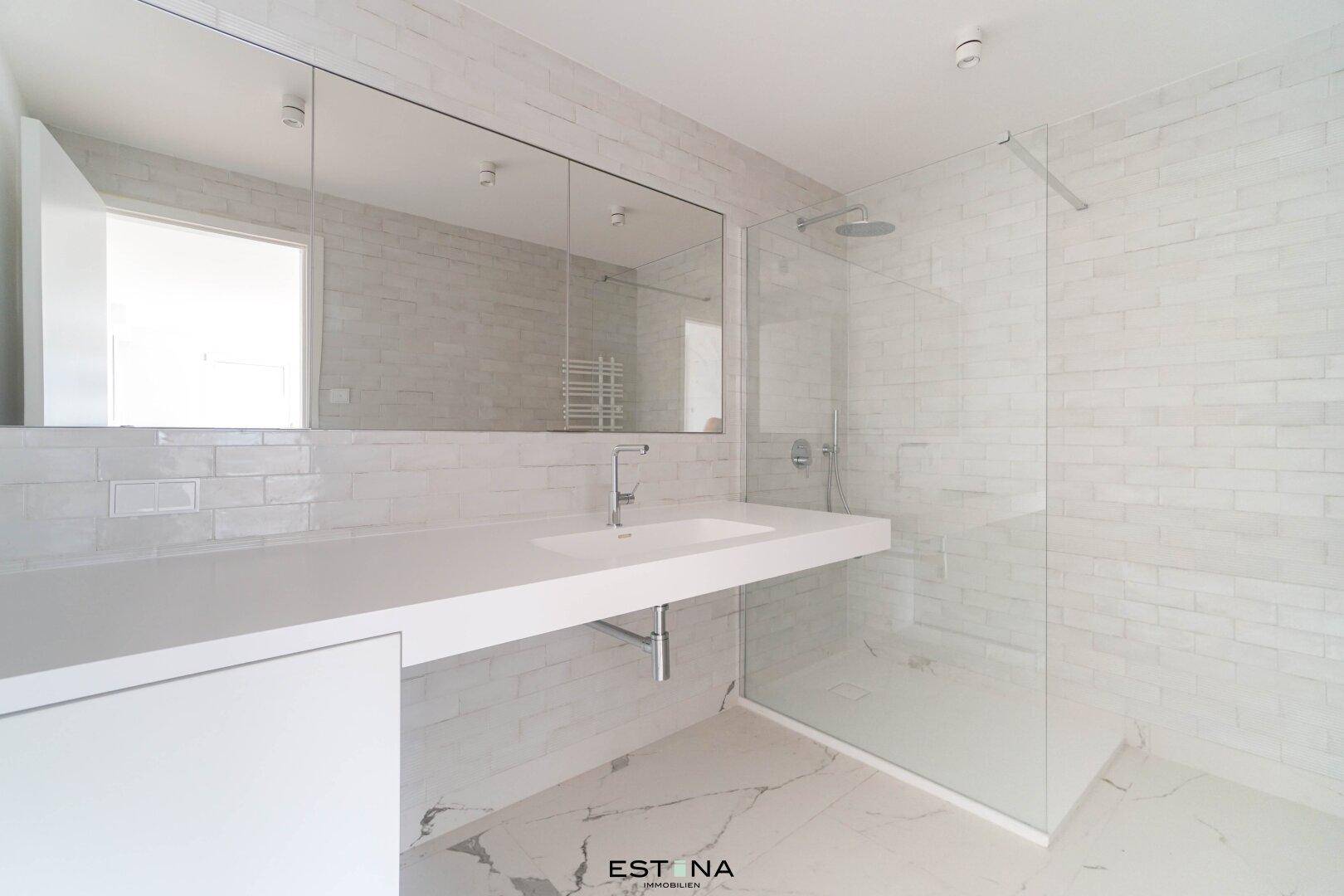 Modernes Badezimmer mit großer begehbarer Dusche, weißem Waschtisch und hellen Fliesen.