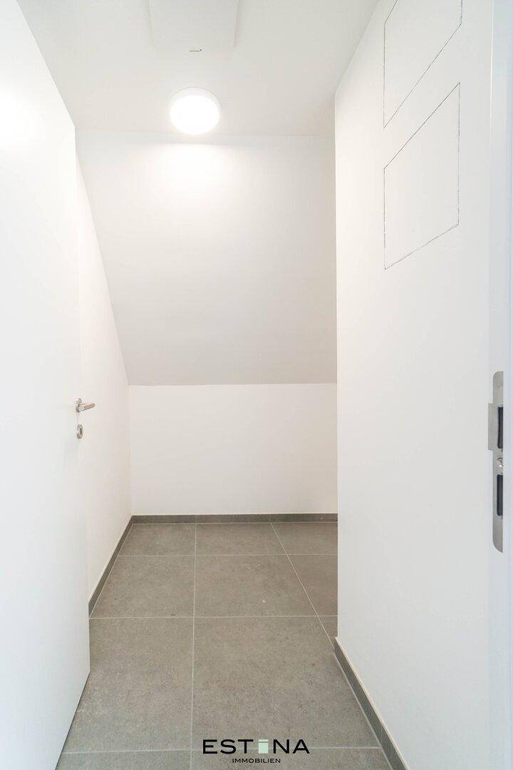 Heller Flur mit grauen Fliesen und einer schrägen Wand, die Stauraum andeutet.