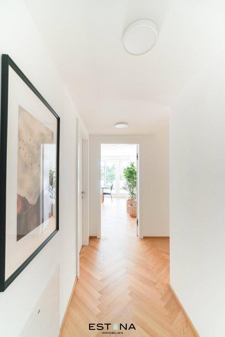 Heller Flur mit Fischgrätparkett, der zu einem lichtdurchfluteten Wohnbereich führt.