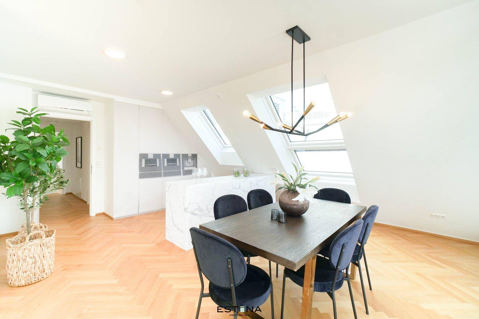Essbereich mit Holztisch, Samtstühlen und moderner Kücheninsel unter Dachfenstern.