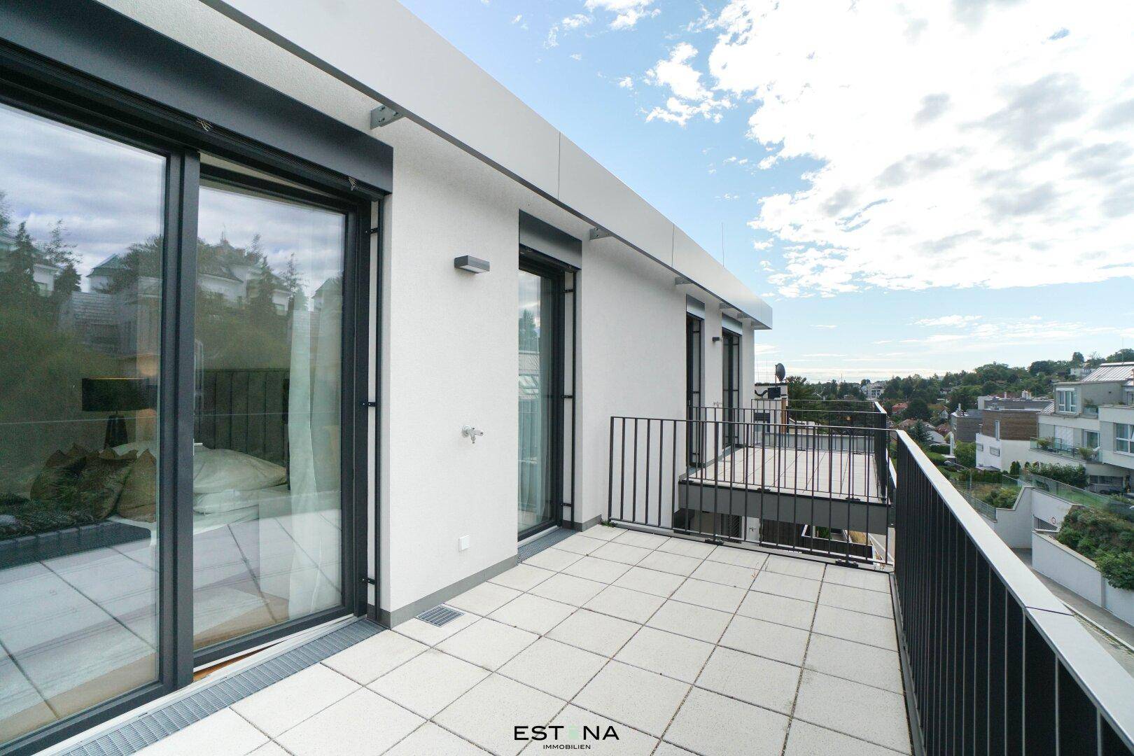 Balkon mit großen Fenstern zum Innenraum und Blick auf die umliegende Bebauung.