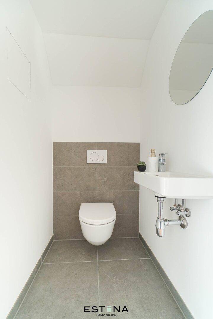 Modernes Gäste-WC mit Wand-WC, kleinem Waschbecken und grauen Wandfliesen.