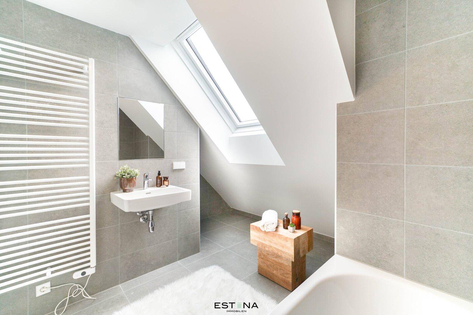 Helles Badezimmer mit Badewanne, Waschbecken, Handtuchheizkörper und Dachfenster.