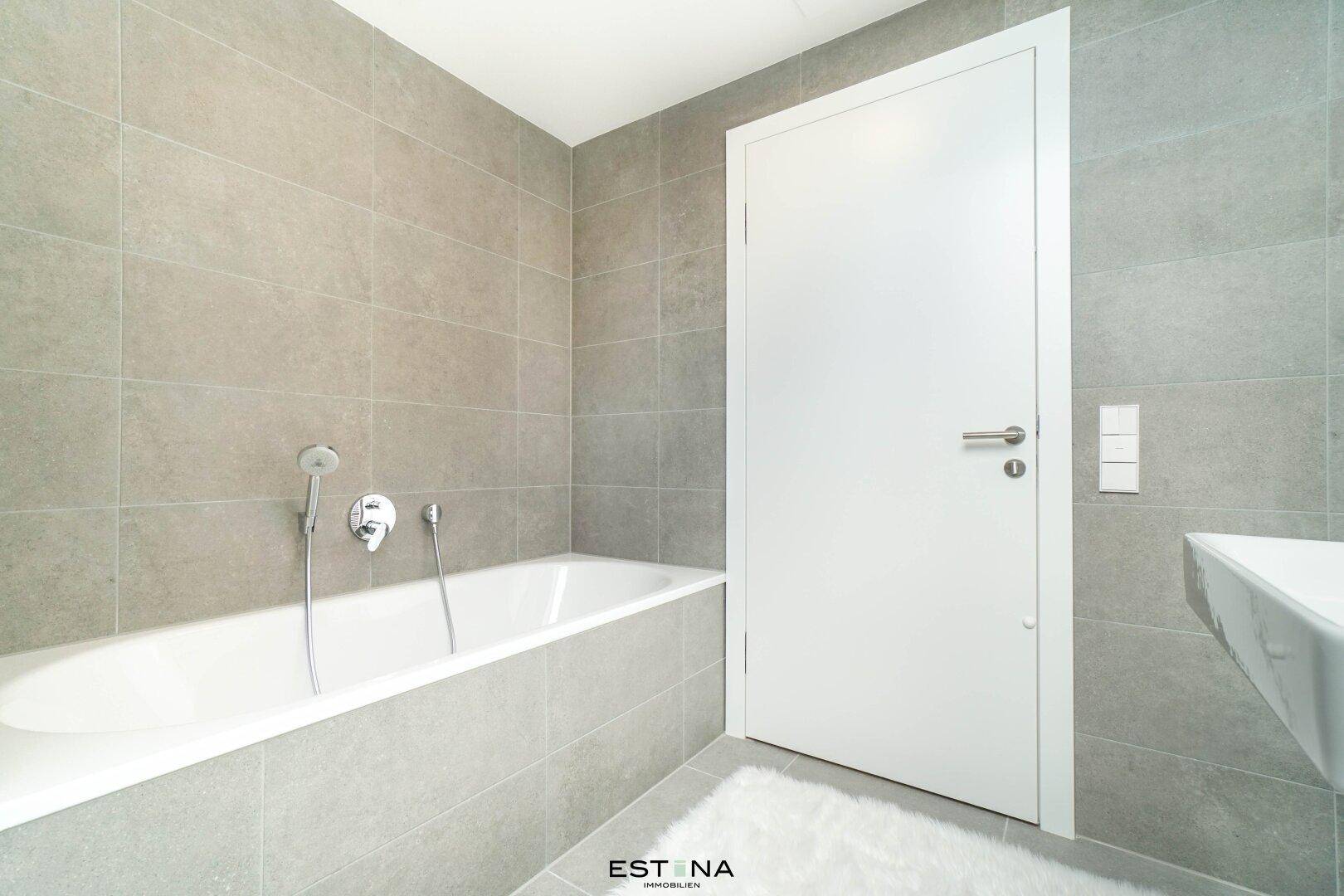 Modernes Badezimmer mit Badewanne und weißer Tür, gefliest in neutralen Farbtönen.