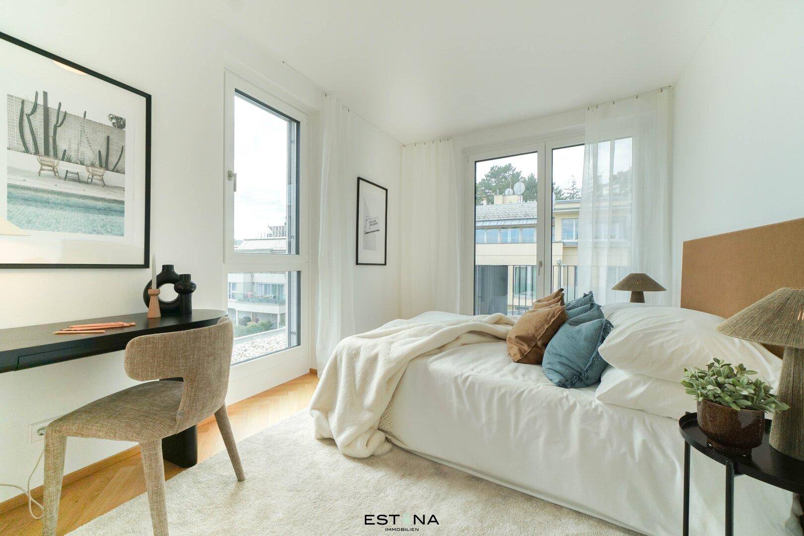 Helles Schlafzimmer mit Bett, Schreibtisch und großen Fenstern mit Blick nach draußen.