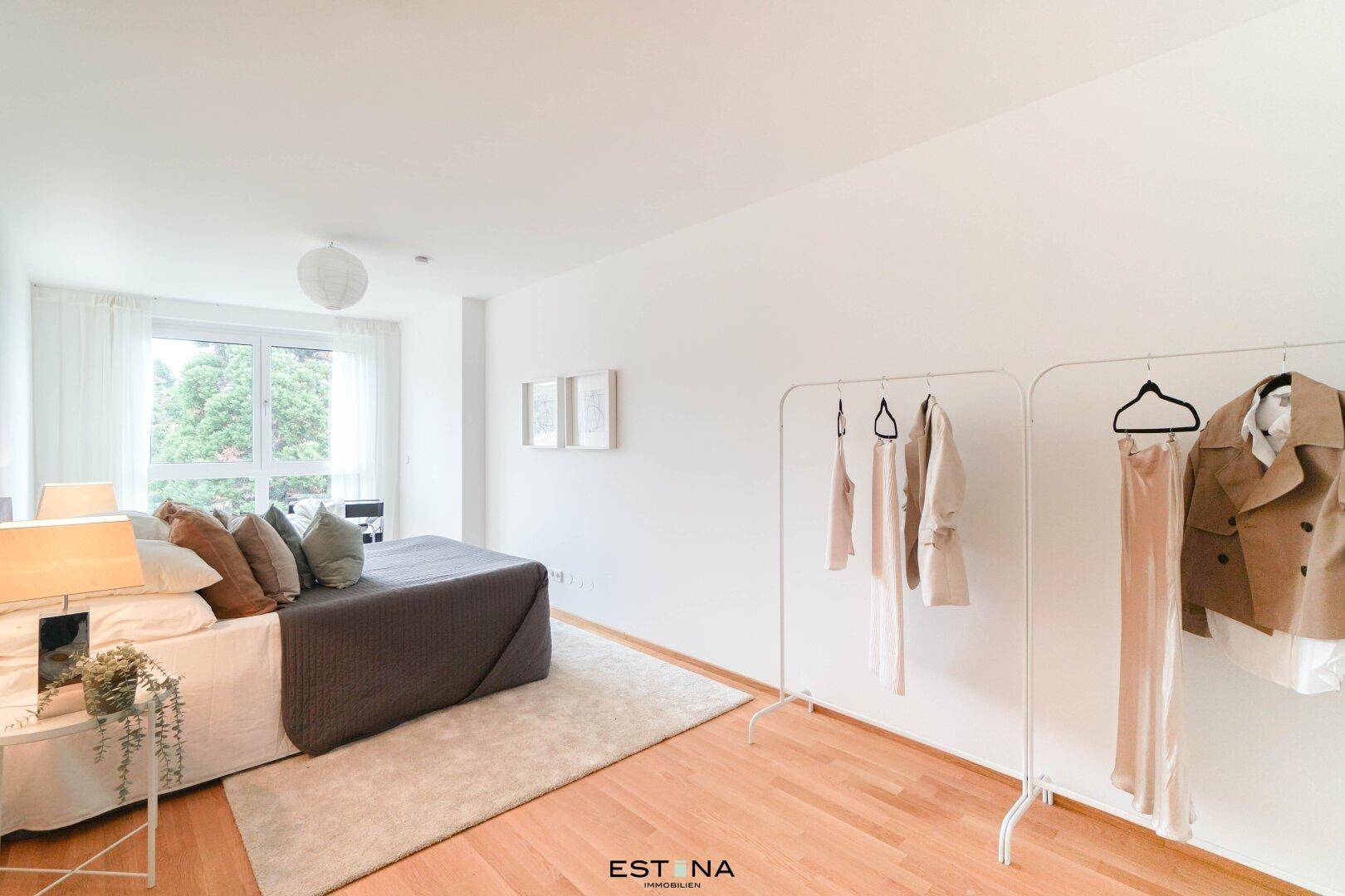 Helles Schlafzimmer mit Doppelbett, Kleiderstangen und großen Fenstern.