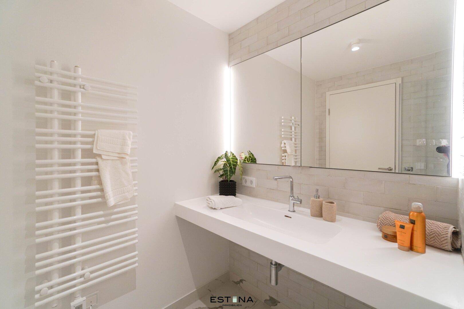 Helles Badezimmer mit modernem Waschbecken, beheiztem Handtuchhalter und Spiegelschrank.