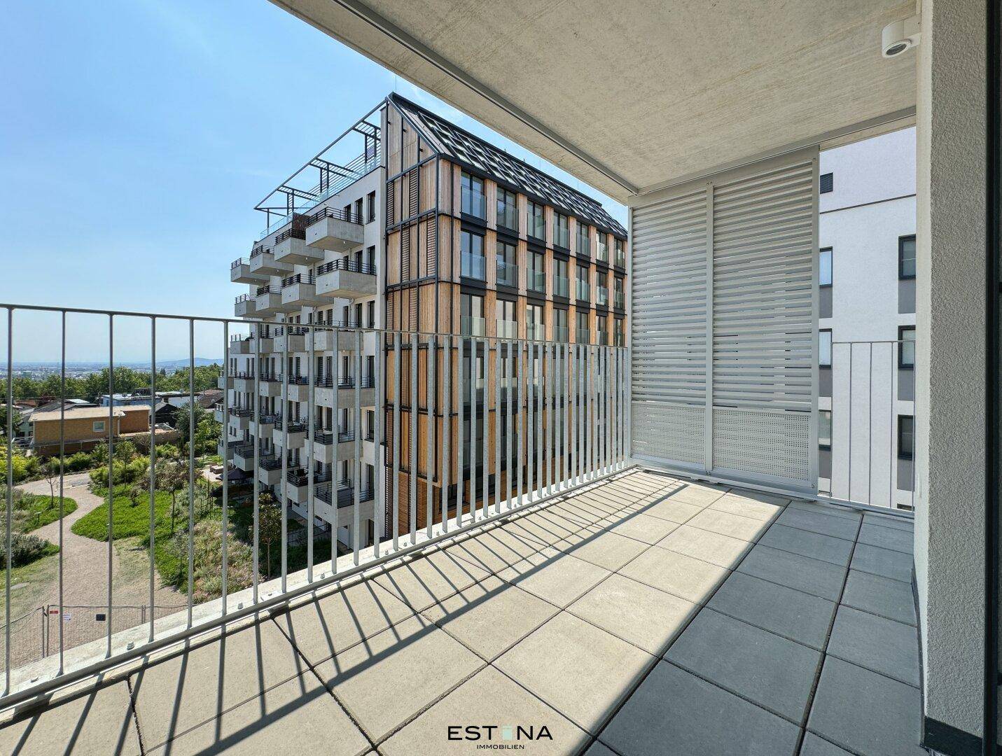 Geräumiger Balkon mit Fliesenboden und weitem Blick auf moderne Gebäude und die Landschaft.