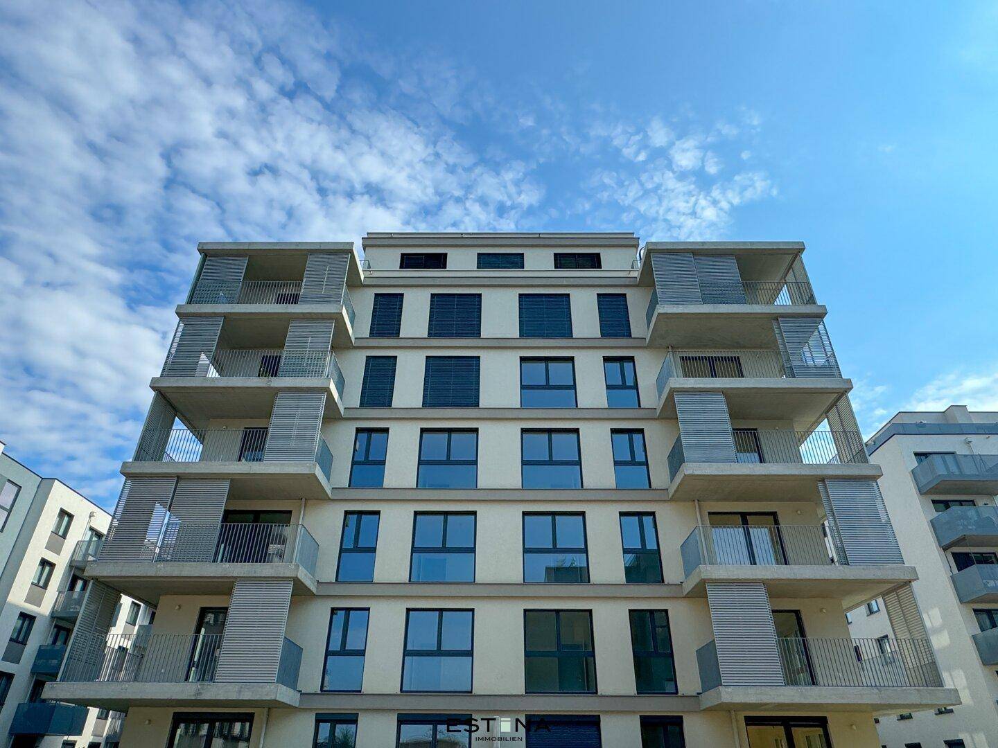 Moderne Fassade eines Neubaus mit großen Fenstern und Balkonen unter blauem Himmel.