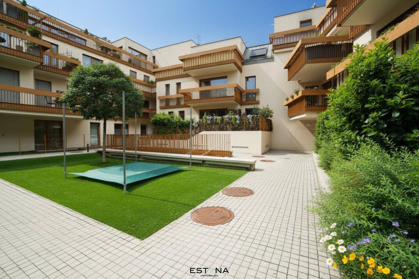Moderner Apartmentkomplex mit mehreren Balkonen, einem begrünten Innenhof und gepflasterten Wegen.