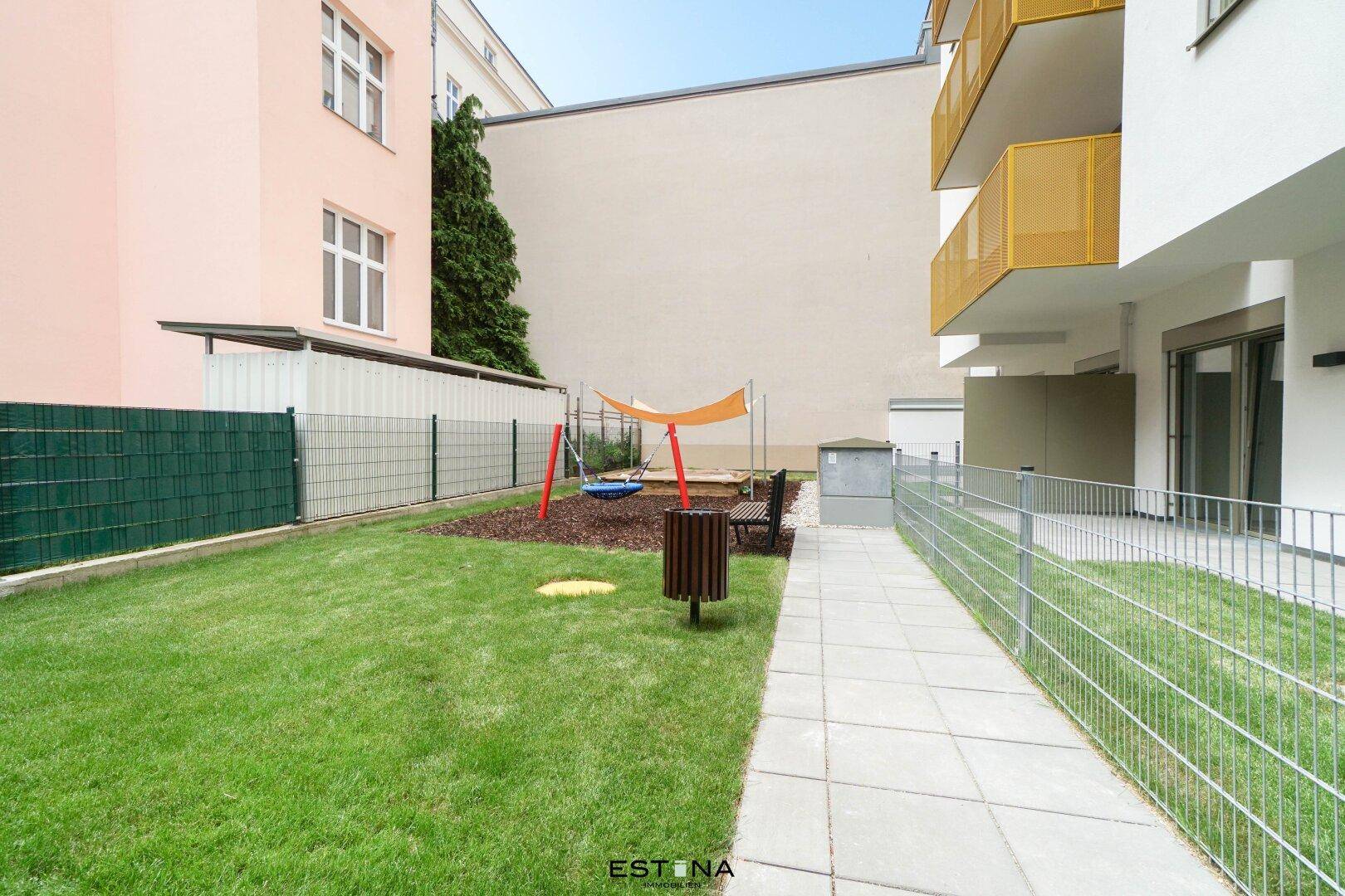 Kinderspielplatz mit Sandkasten und Schaukel, umgeben von einer Rasenfläche.