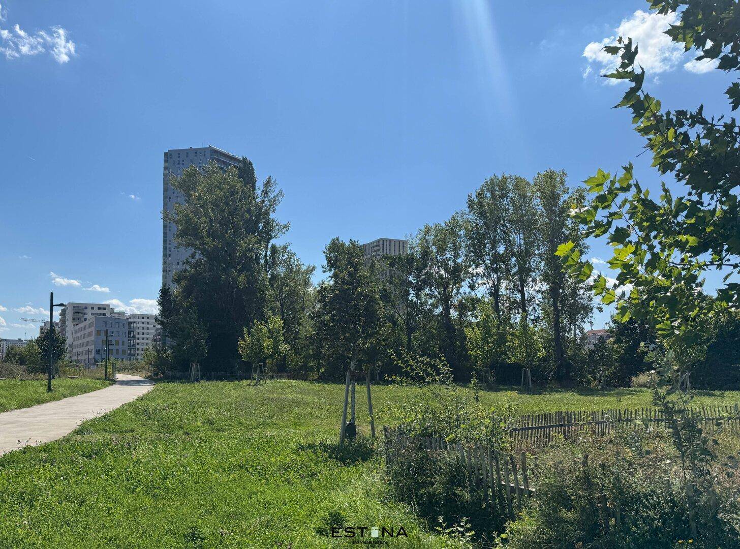 Grüne Parklandschaft mit Bäumen und modernen Gebäuden im Hintergrund.