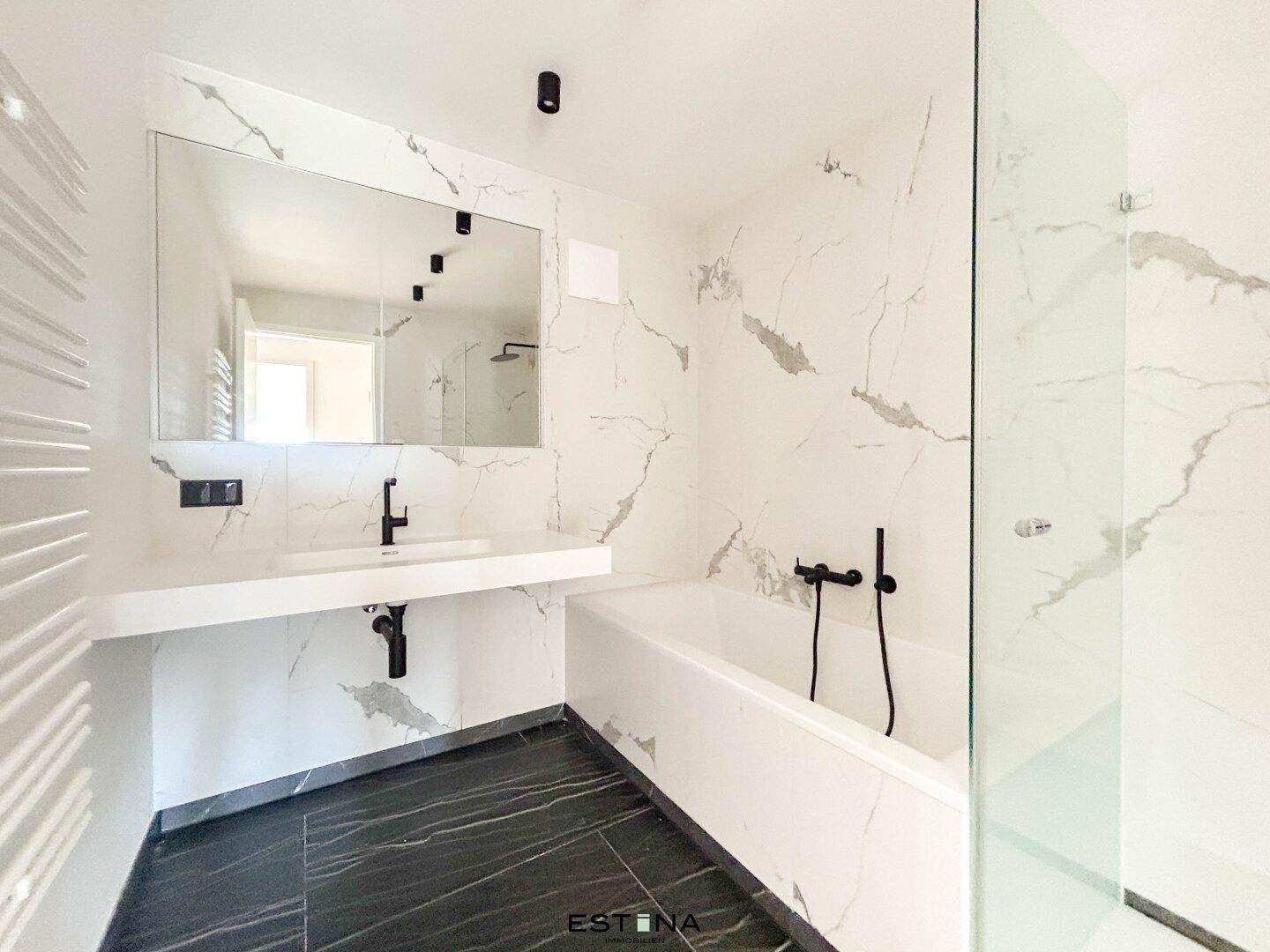 Elegantes Badezimmer mit Marmoroptik-Fliesen, moderner Badewanne und separater Dusche mit schwarzen Armaturen.