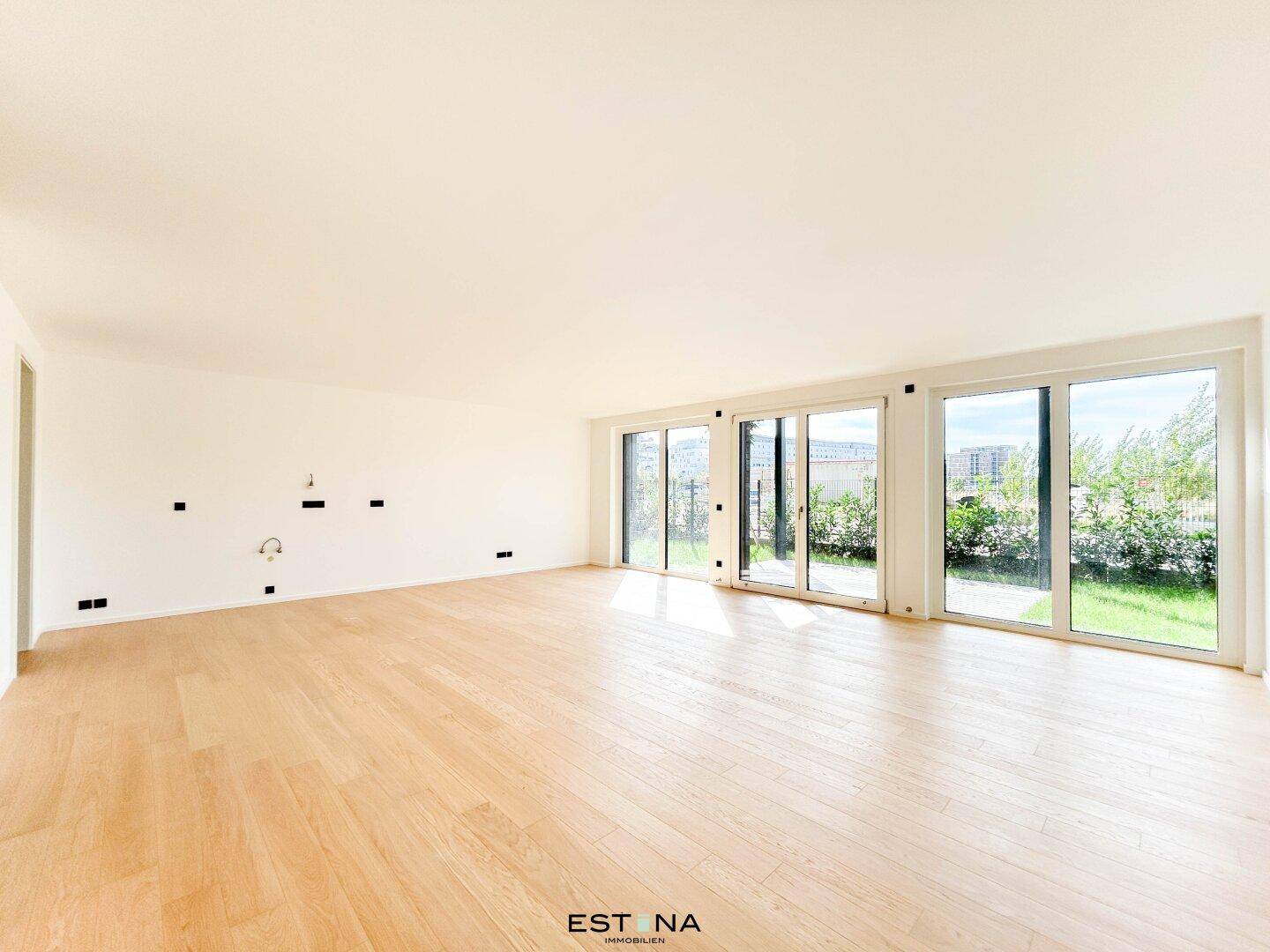 Heller, leerer Wohnraum mit Eichenparkett und großen Fensterfronten, die viel Tageslicht hereinlassen.