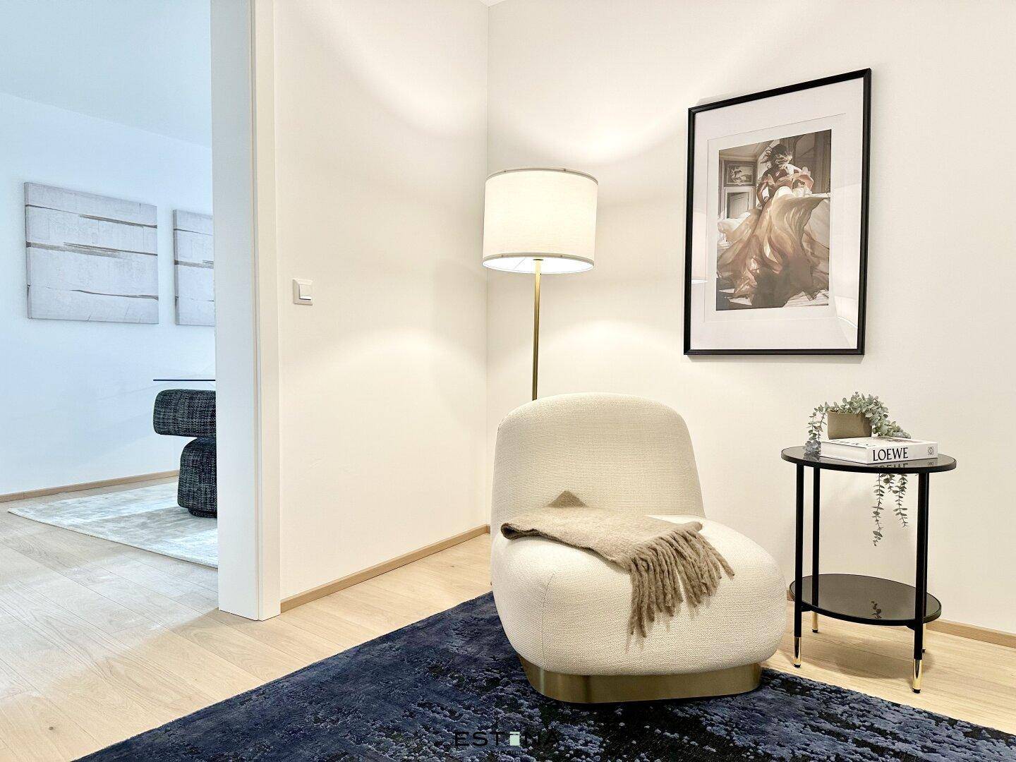Heller Flurbereich mit stilvollem Sessel, Stehlampe und Kunstwerk an der Wand.