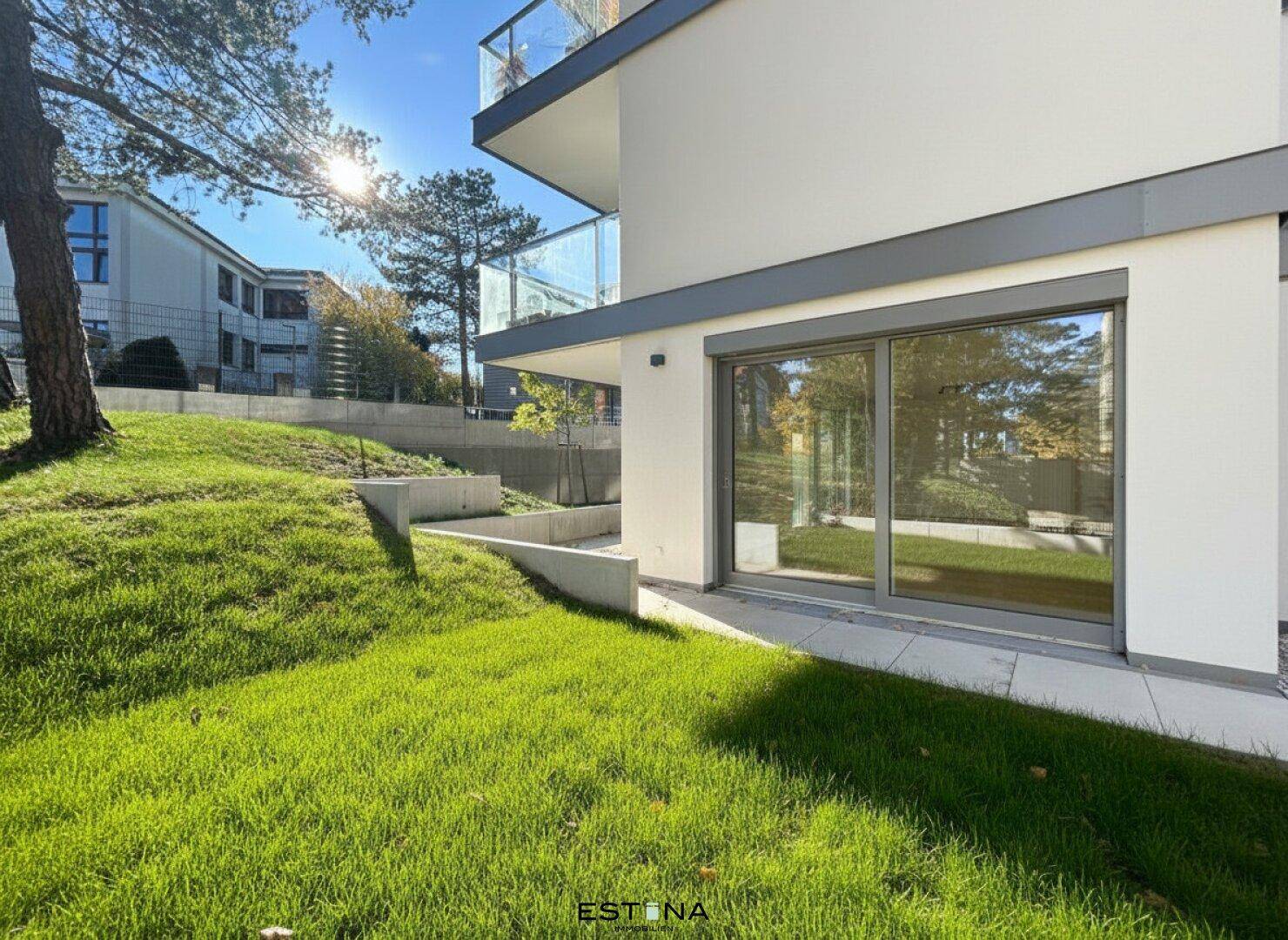 Moderne Gebäudefassade mit großen Fenstern und angrenzender Rasenfläche unter blauem Himmel.