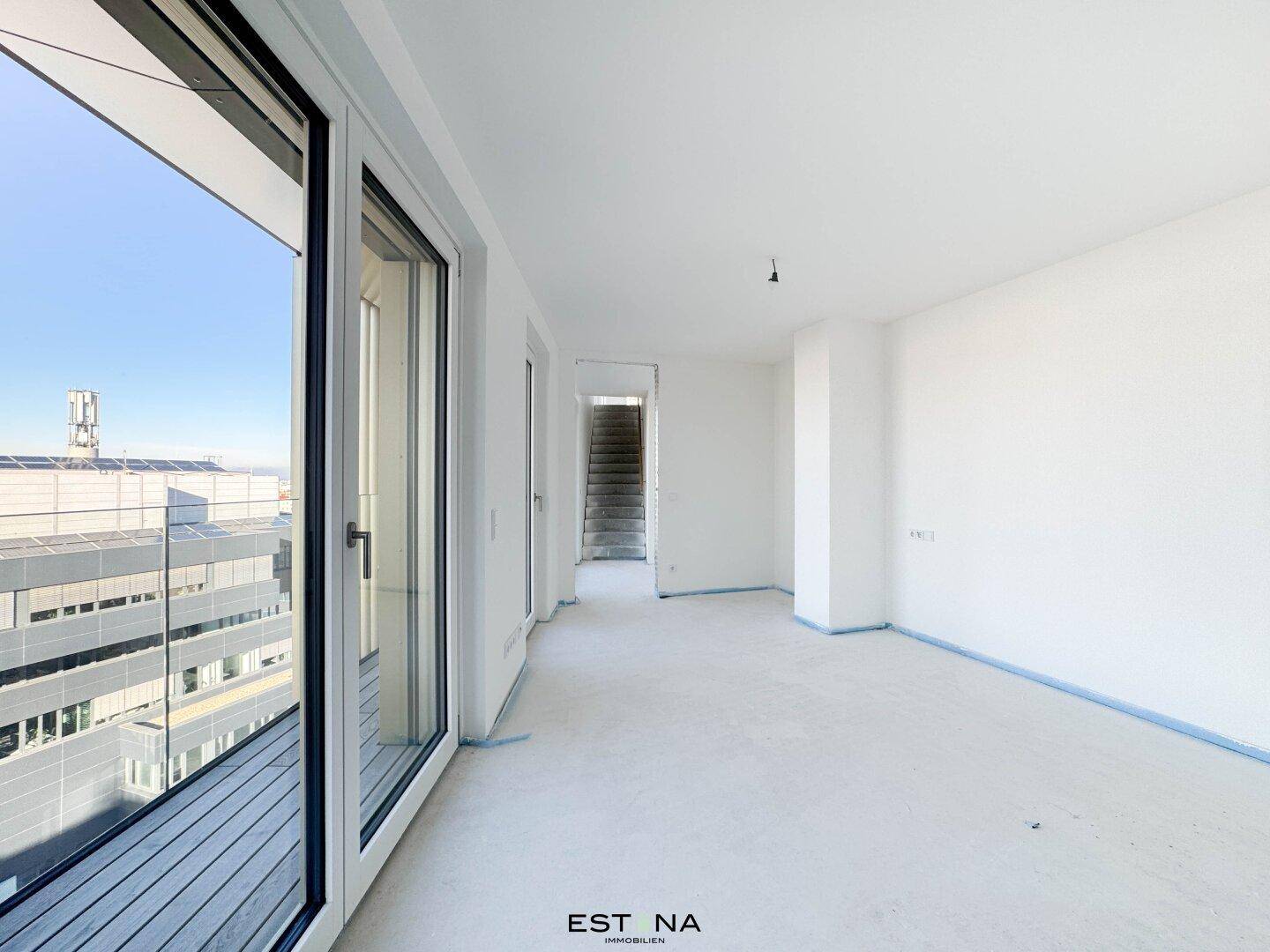 Heller Flur mit großen Fenstern und Zugang zu einem Balkon, führt zu einer Treppe.
