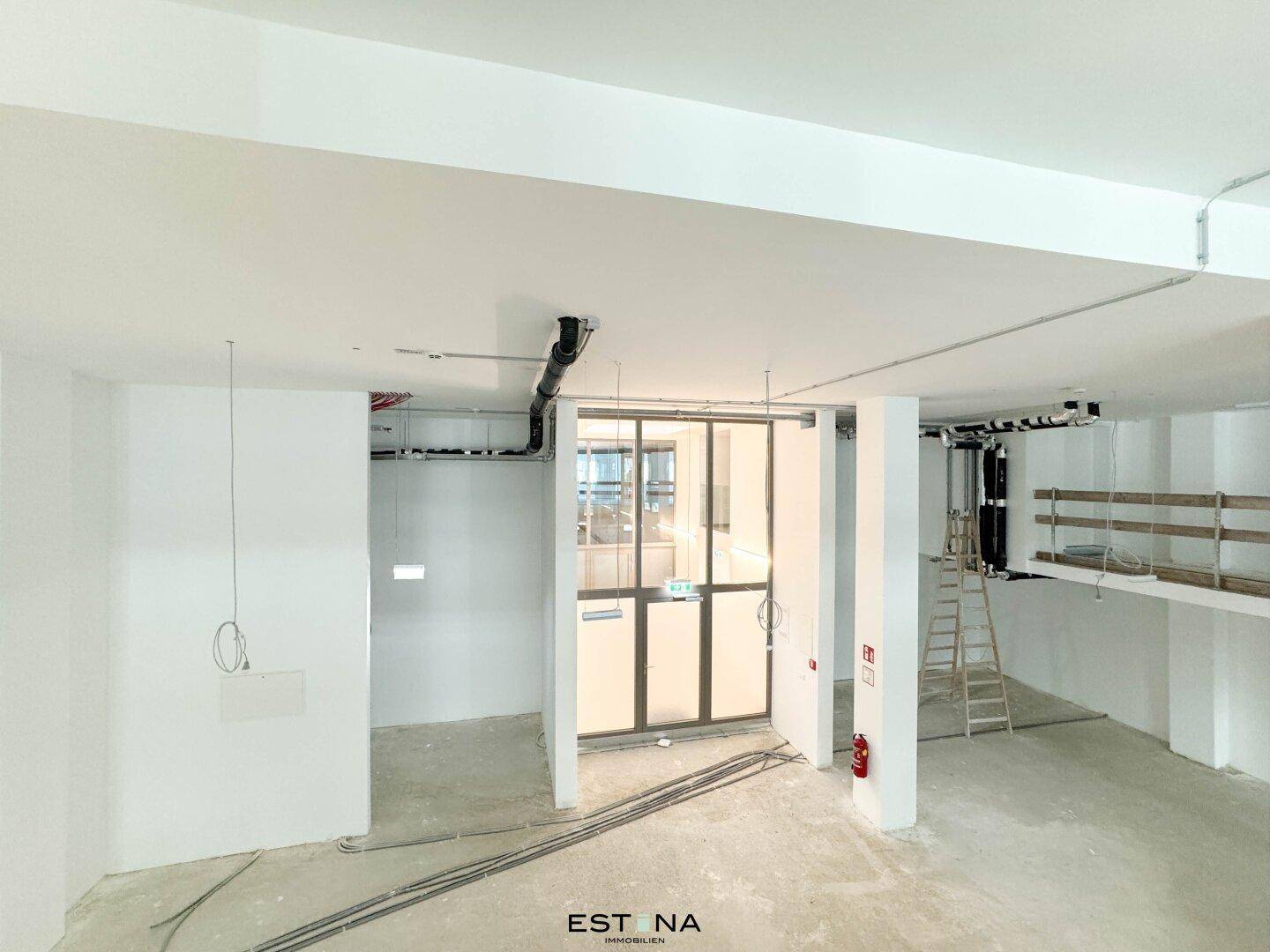 Unfertiger Innenraum mit sichtbaren Leitungen und einer Glastür, bereit für den Ausbau.