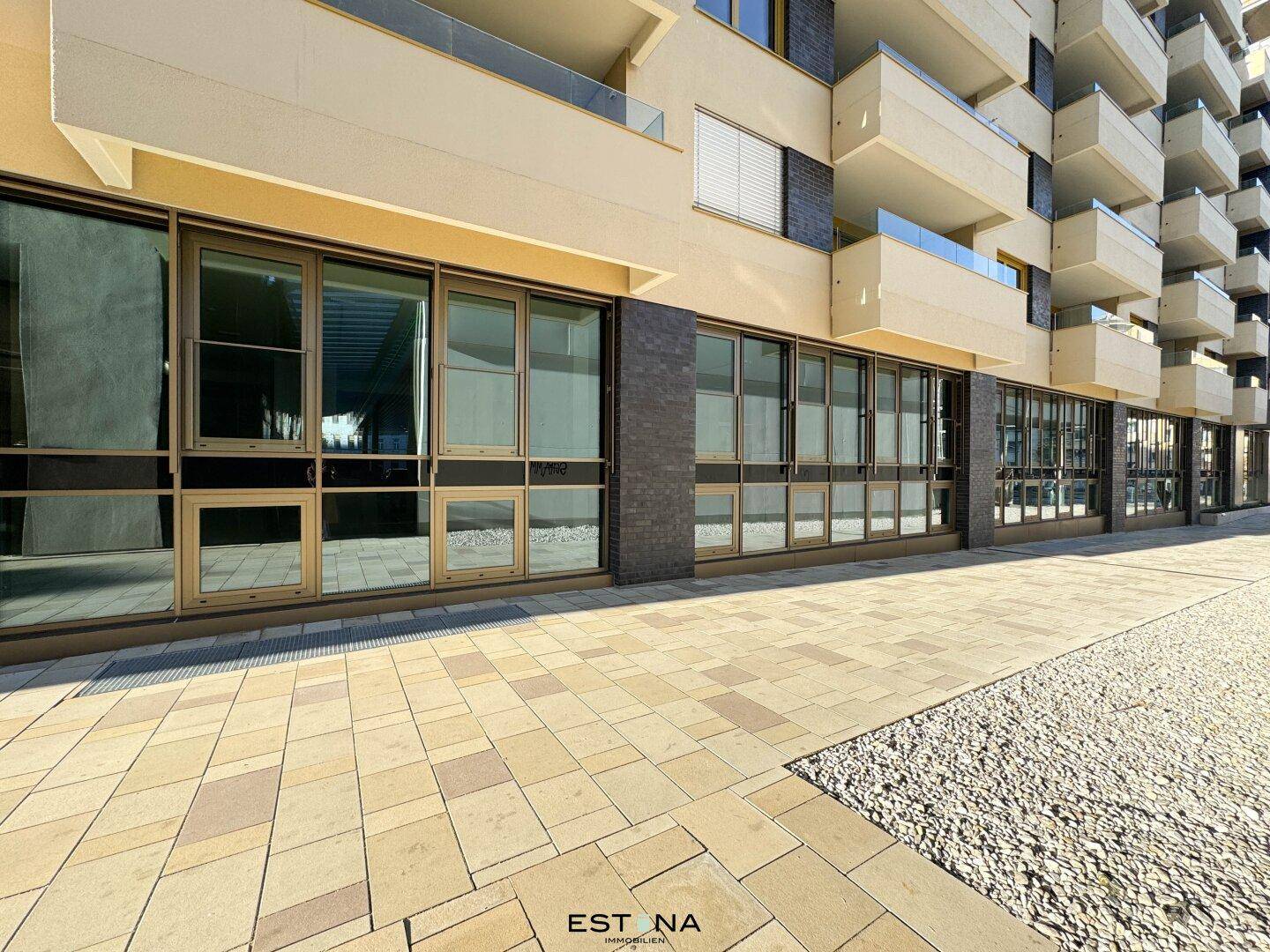 Erdgeschossfassade eines modernen Gebäudes mit großen Schaufenstern und gepflastertem Gehweg.