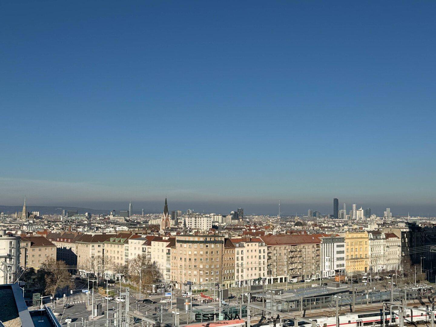 Weitläufiger Panoramablick über die Dächer der Stadt unter einem klaren blauen Himmel.