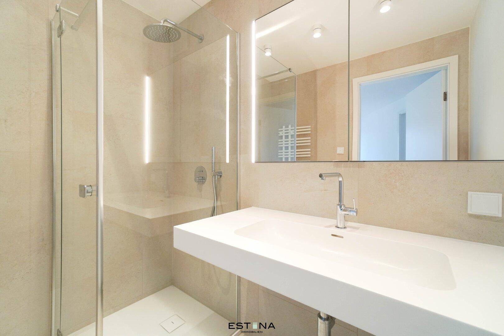 Modernes Badezimmer mit begehbarer Dusche, eleganten Fliesen und beleuchtetem Spiegelschrank.