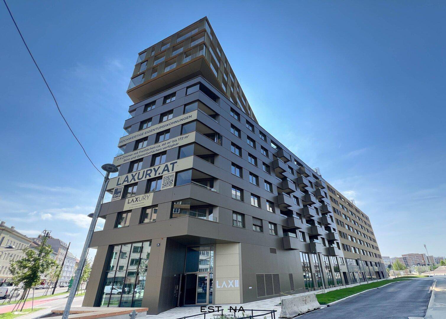 Modernes Apartmentgebäude mit markanter Architektur und zahlreichen Balkonen unter blauem Himmel.