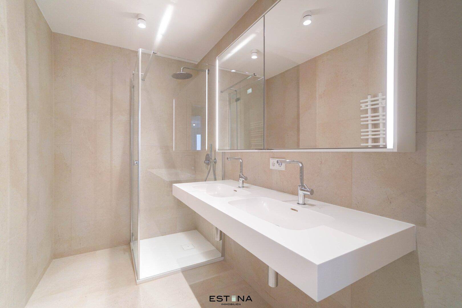Modernes Badezimmer mit Doppelwaschbecken, großer Dusche und hellen Fliesen.