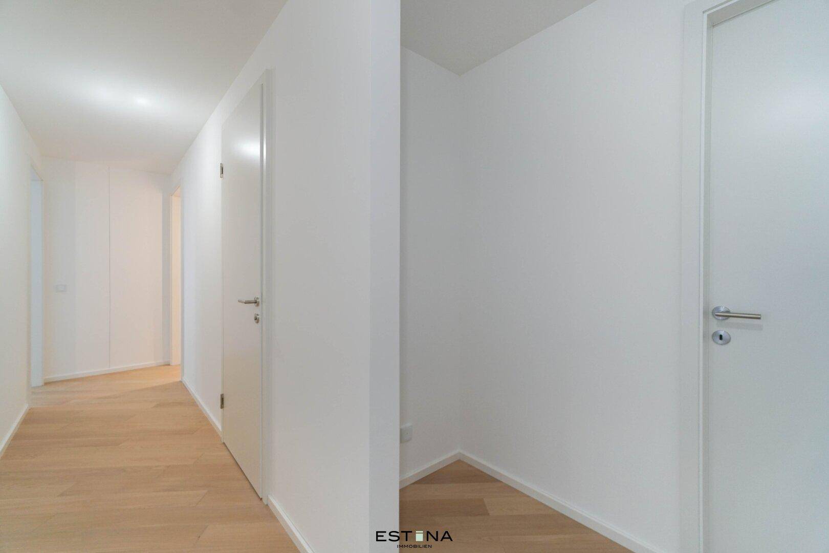 Heller Flur mit Holzboden und weißen Wänden, der zu weiteren Räumen führt.