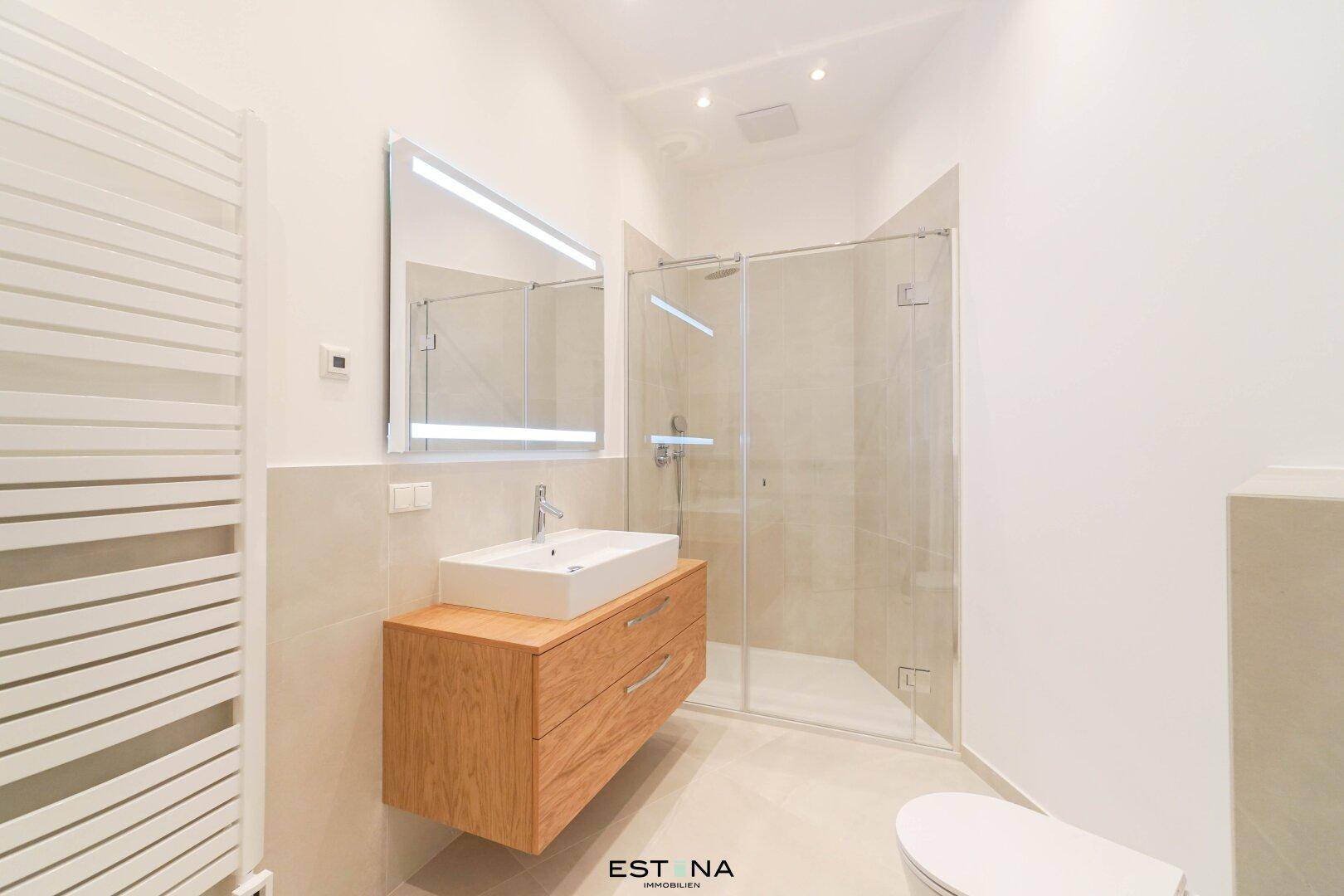 Modernes Badezimmer mit schwebendem Waschtisch, begehbarer Dusche und beheiztem Handtuchhalter.