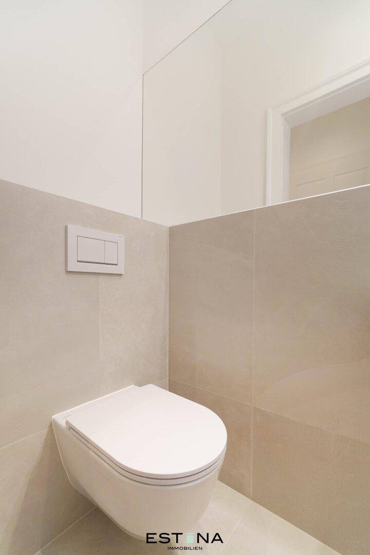 Modernes Gäste-WC mit wandhängender Toilette und großem Spiegel, in hellen Fliesen gehalten.