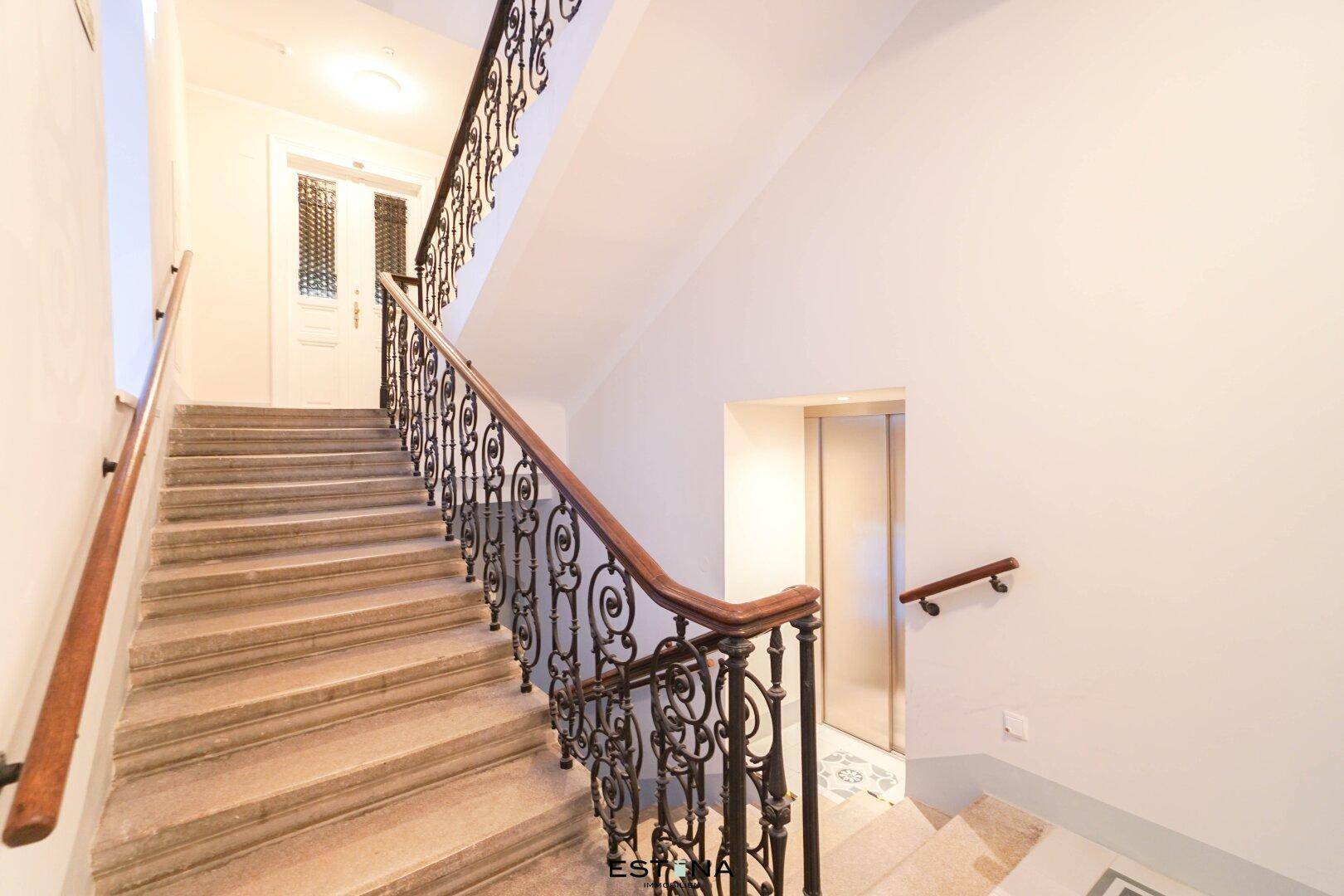 Elegantes Treppenhaus mit schmiedeeisernem Geländer und Holzhandlauf, inklusive Aufzugzugang.