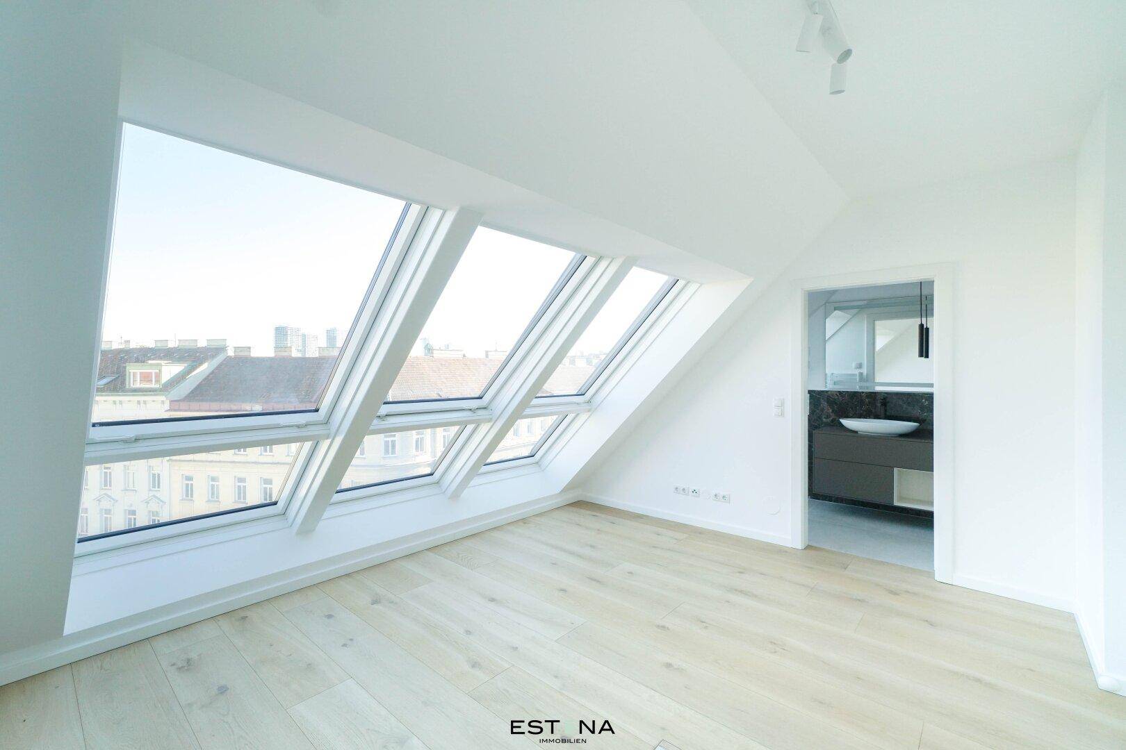 Helles Schlafzimmer im Dachgeschoss mit großen Fenstern und Zugang zum Bad.