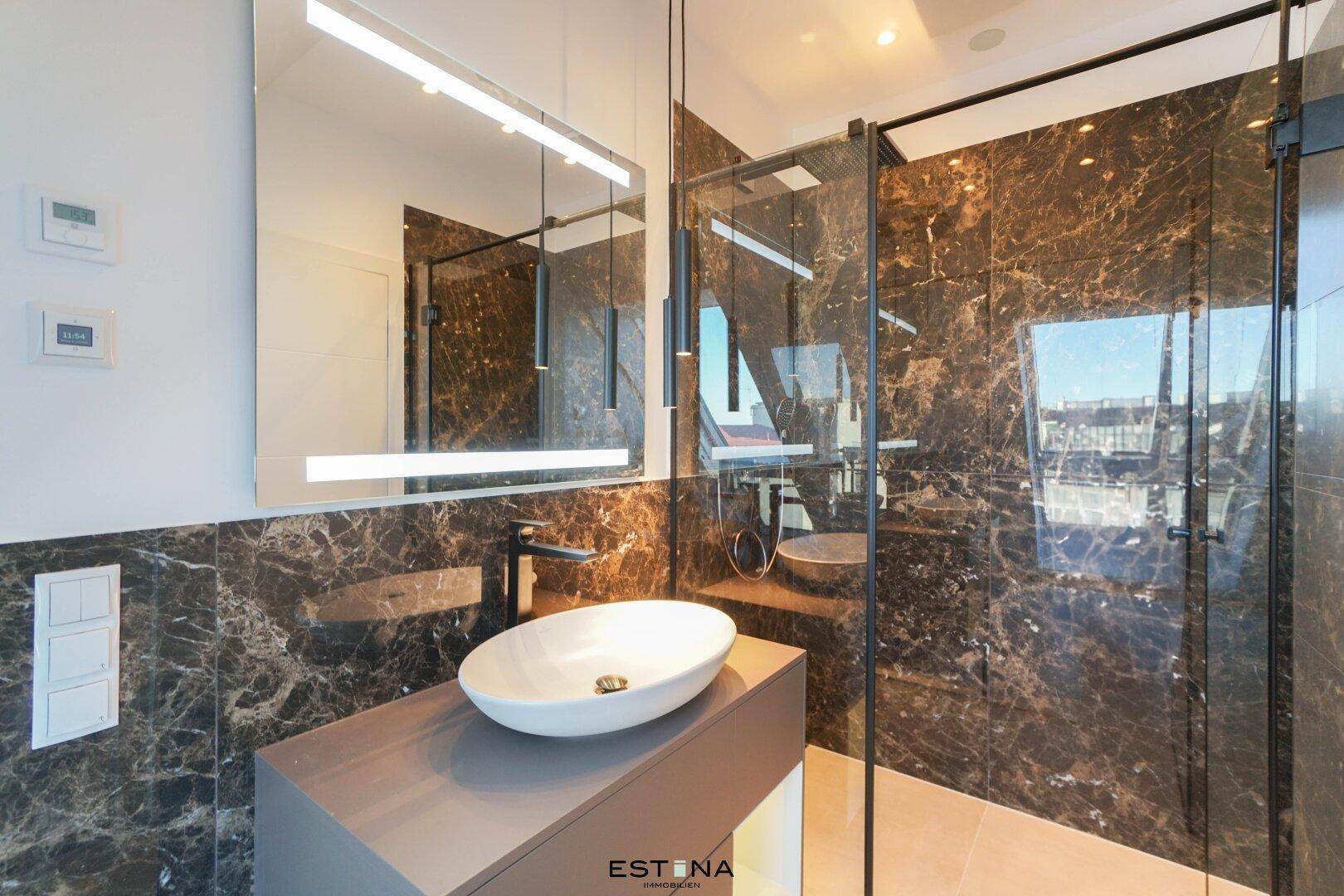 Elegantes Badezimmer mit Marmorwänden, Aufsatzwaschbecken und großer Spiegelfläche.