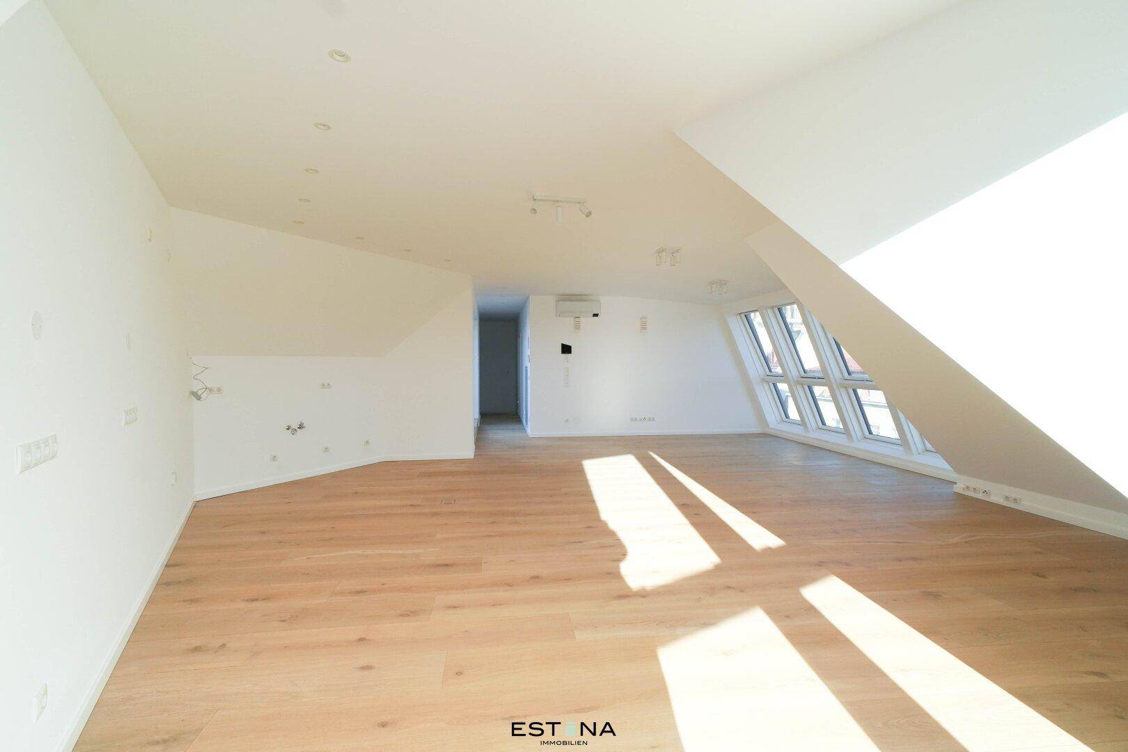 Heller, leerer Wohnraum im Dachgeschoss mit schrägen Wänden und Holzboden.