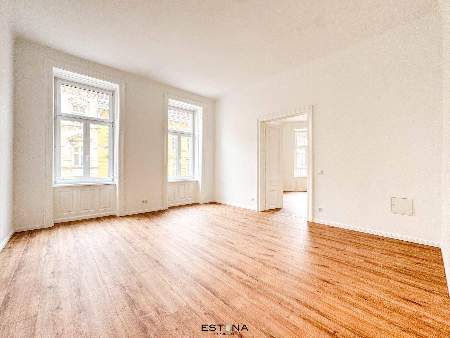 Heller Wohnbereich mit Holzboden und Flügeltüren, die zu einem weiteren Raum führen und viel Potenzial bieten.