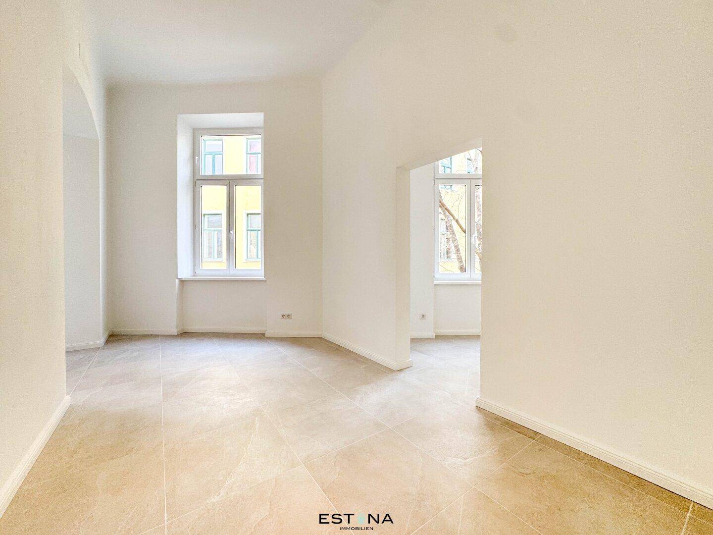 Heller Raum mit beigefarbenen Fliesen und hohen Fenstern, die viel Licht spenden und eine moderne Basis bilden.