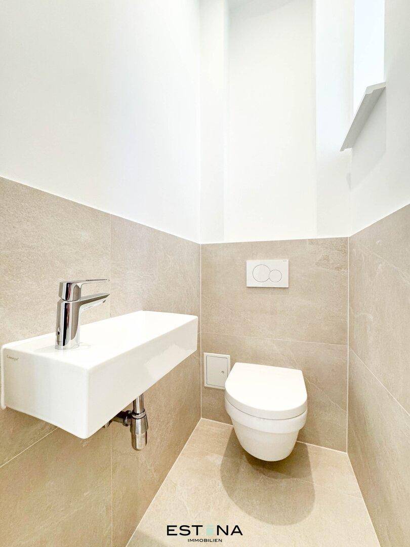 Modernes Gäste-WC mit wandhängendem Waschbecken und Toilette, hell gefliest und sehr gepflegt.