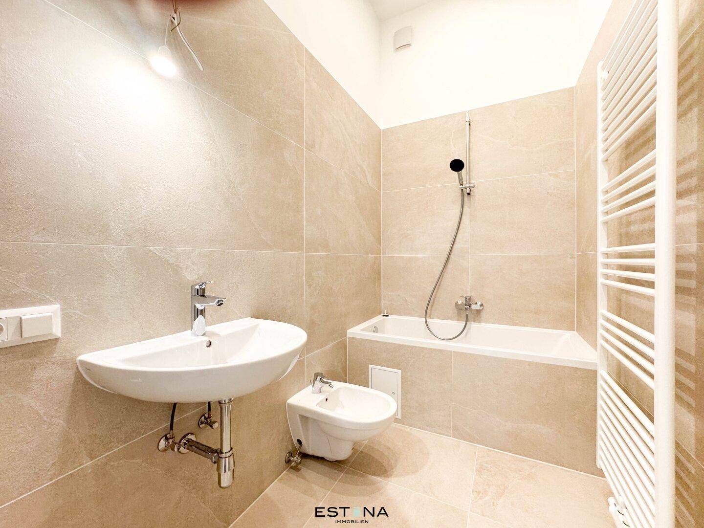 Modernes Badezimmer mit Badewanne, Waschbecken und Bidet, komplett gefliest in Beige und gut gepflegt.