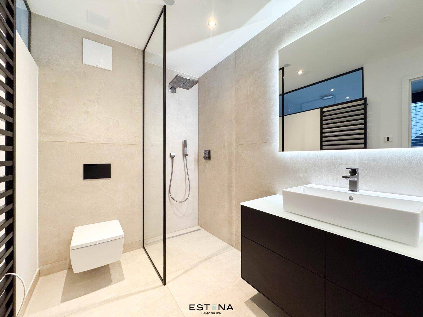 Modernes Badezimmer mit begehbarer Dusche, schwebendem Waschtisch und beleuchtetem Spiegel.
