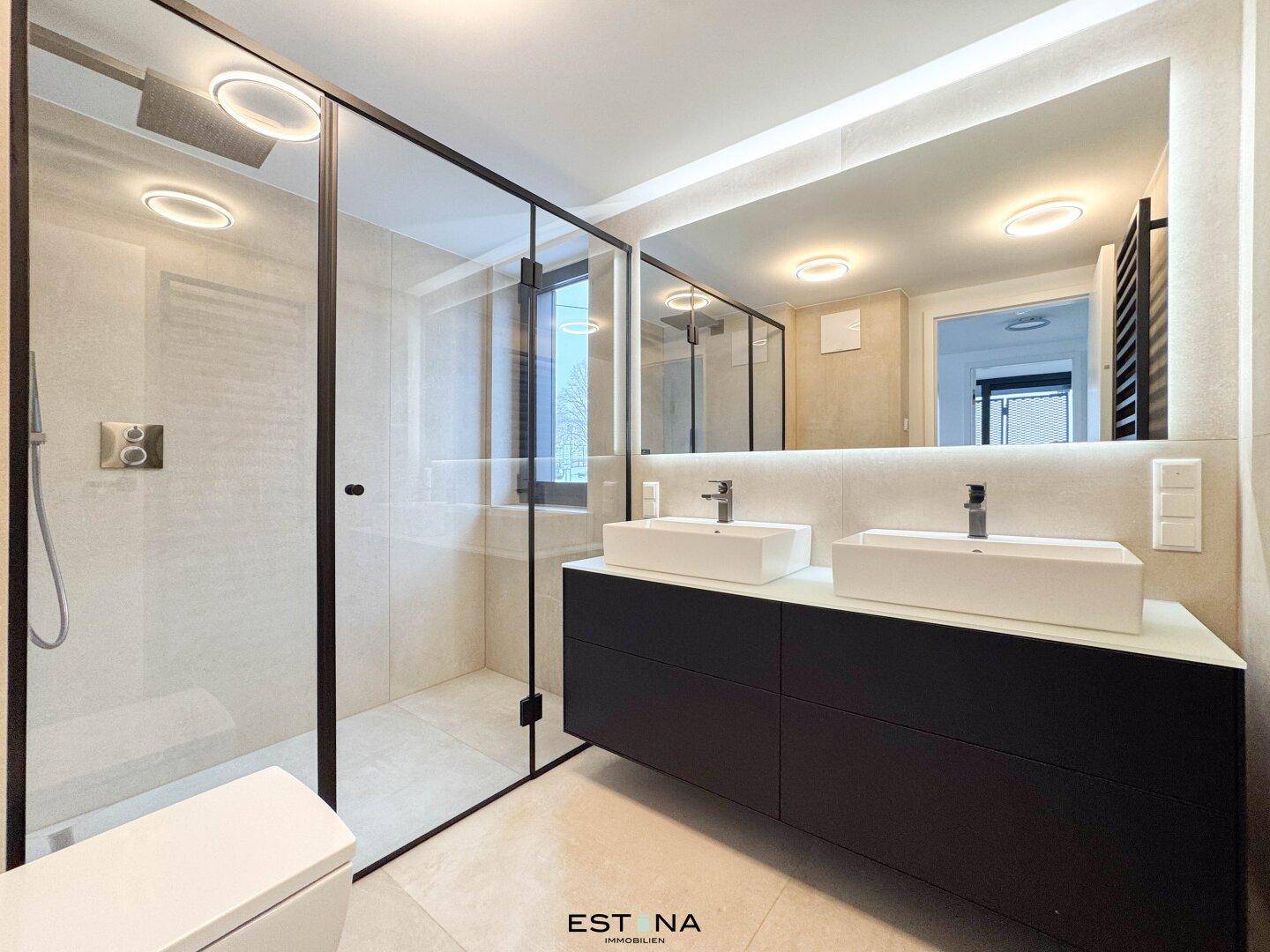 Luxuriöses Badezimmer mit Doppelwaschbecken, großer begehbarer Dusche und beleuchtetem Spiegel.