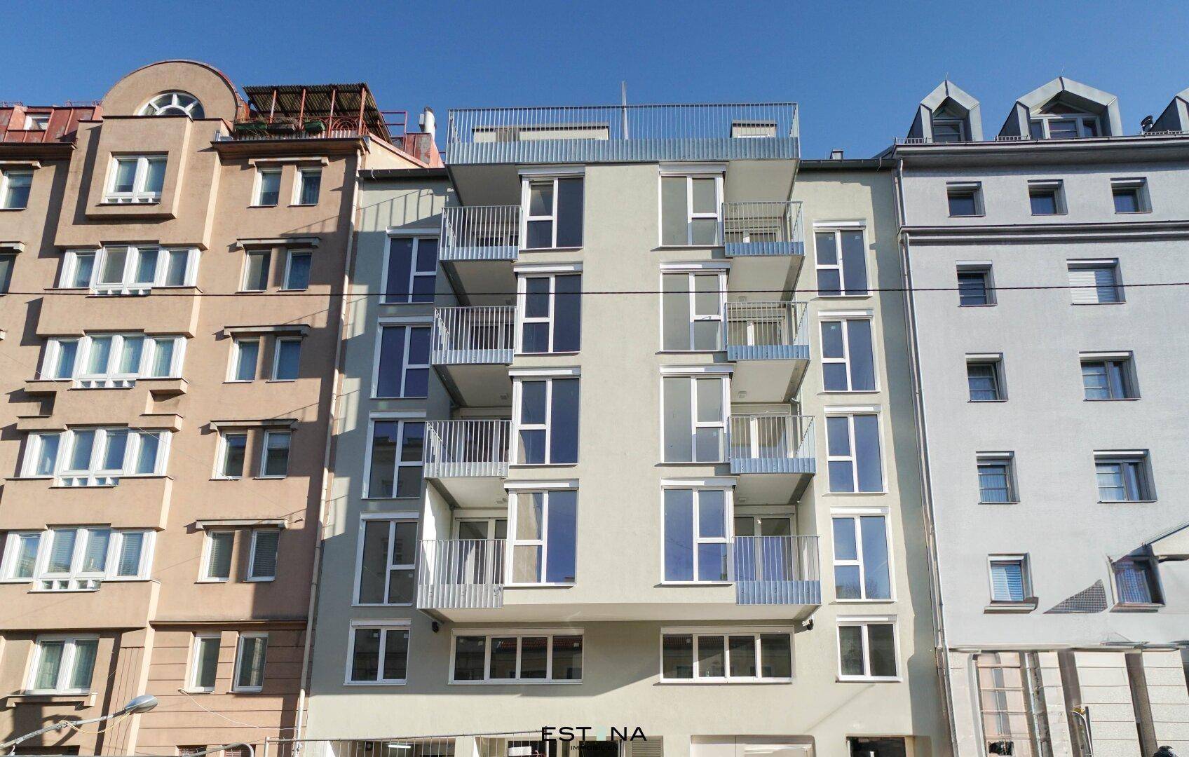 Moderne Wohnhausfassade mit zahlreichen Balkonen und großen Fenstern in einer städtischen Umgebung.