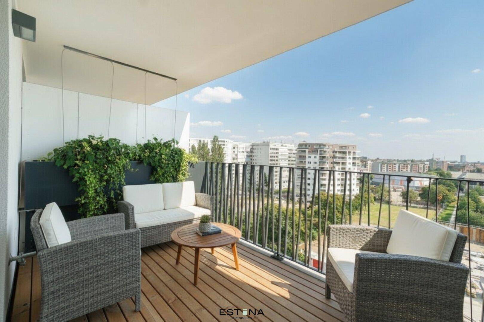 Möblierter Balkon mit Holzboden, Pflanzen und weitem Blick über die Stadt.