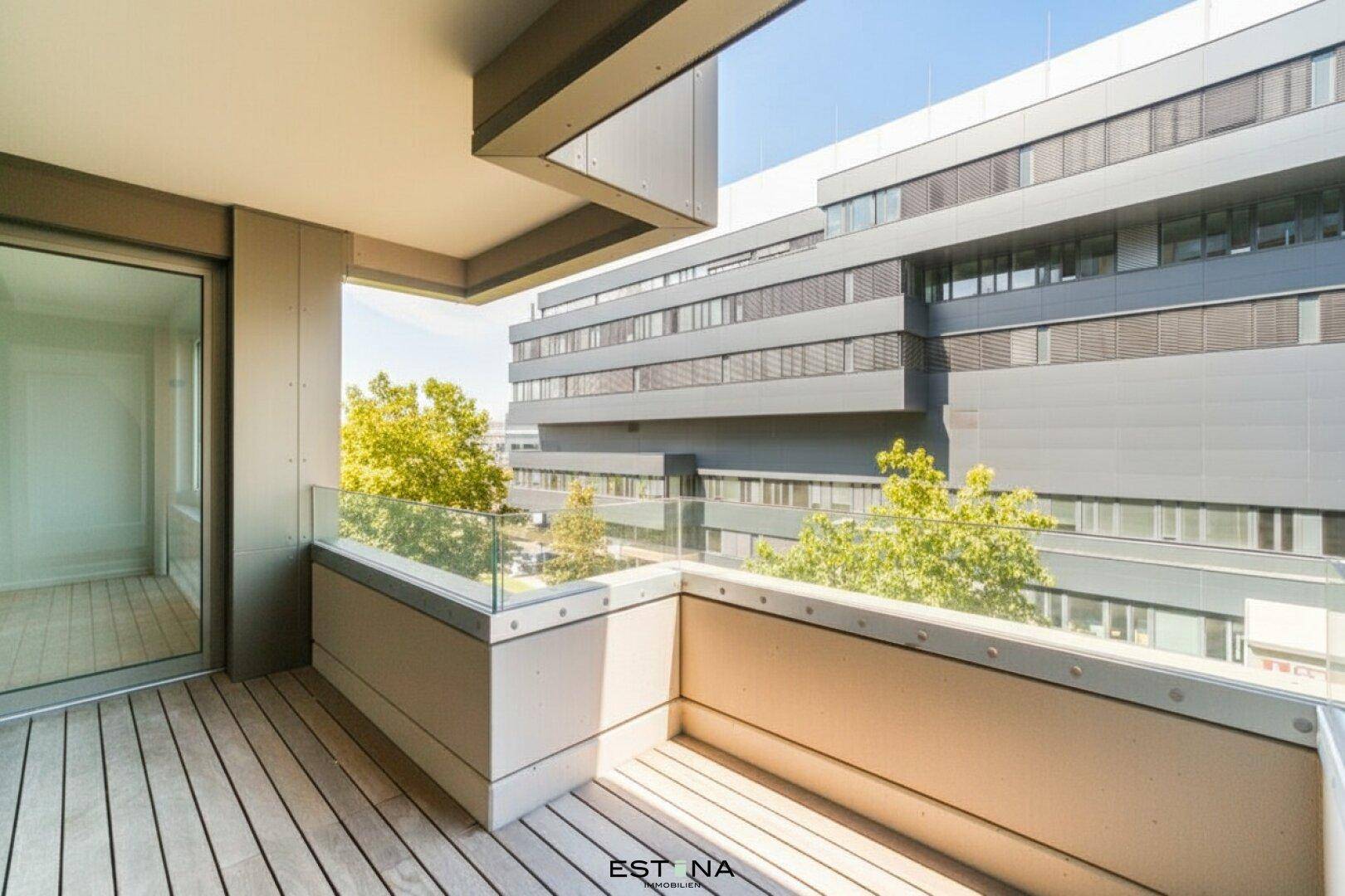 Geräumiger Balkon mit Holzboden und Glasgeländer, umgeben von moderner Architektur.